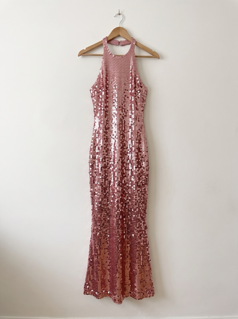 Plain photo of a pink sequin halter gown on a wooden hanger against a white wall